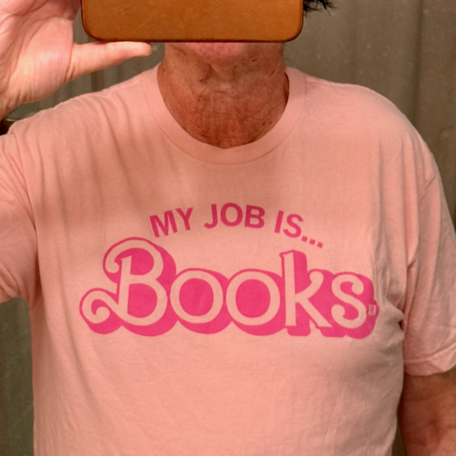 photo of editor Mikesch Muecke wearing a pink t-shirt that says My Job is Books. His face is hidden behind the camera taking the photo
