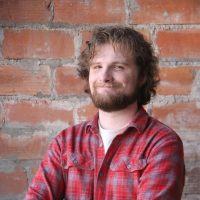 Stewart Chisham wears a red checkered shirt, crossing his arms and smiles at the camera