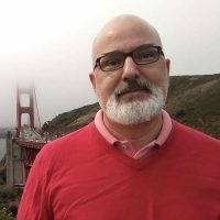 Peter Wodarz, in a red sweater, stands in the landscape north of San Francisco, with the Golden Gate Bridge in the background over his right shoulder
